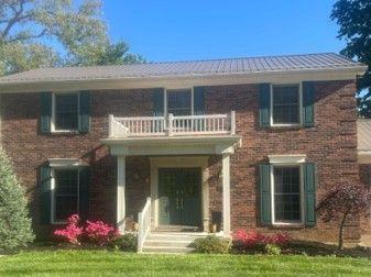 Two-story brick house with white porch, green shutters, and pink flowers in front yard Two-story brick house with white porch, green shutters, and pink flowers in front yard