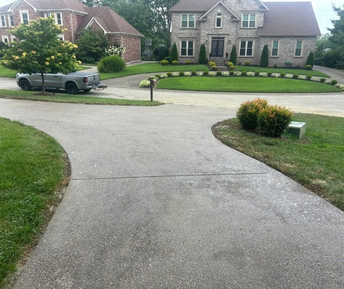 Suburban driveway leading to two brick-and-stone houses, with a pickup truck parked at left.