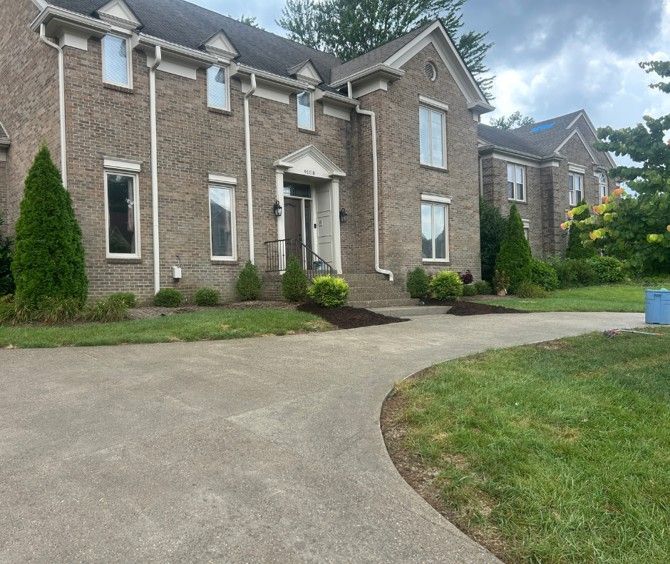 Brick suburban house with curved driveway, front porch, and landscaped lawn under cloudy sky