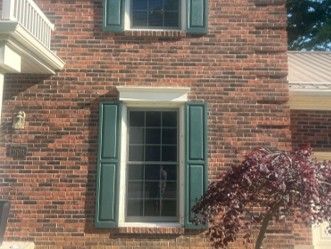 Brick house exterior with a window framed by green shutters and a leafy tree branch in front Brick house exterior with a window framed by green shutters and a leafy tree branch in front