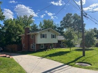Brick-and-white house on a sunny corner lot with a sloped driveway, green lawn, and trees overhead Brick-and-white house on a sunny corner lot with a sloped driveway, green lawn, and trees overhead