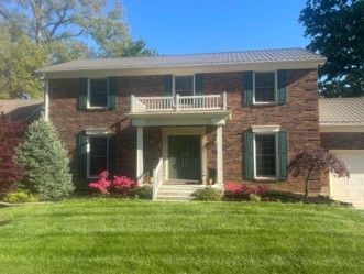 Two-story brick house with a front porch, balcony, and green lawn under a blue sky