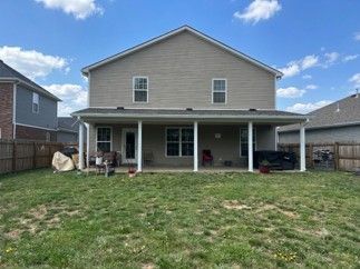 Backyard view of a two-story beige house with a covered patio and lawn under a blue sky