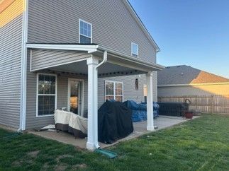 Backyard patio with covered deck, grill, and fenced lawn beside a house