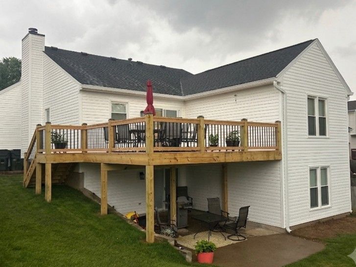 White house with a raised wooden deck, red umbrella, and patio furniture under a cloudy sky.