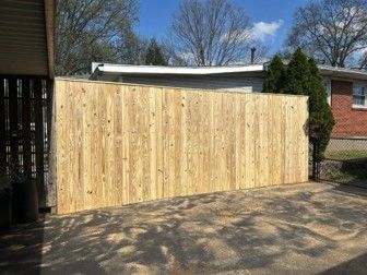 Wooden privacy fence enclosing a driveway beside a house, with trees and blue sky above. Wooden privacy fence enclosing a driveway beside a house, with trees and blue sky above.