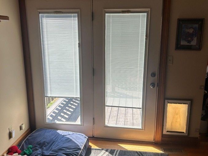 Sunlit room with French doors, blinds, a small dog bed, and a pet door on the right.