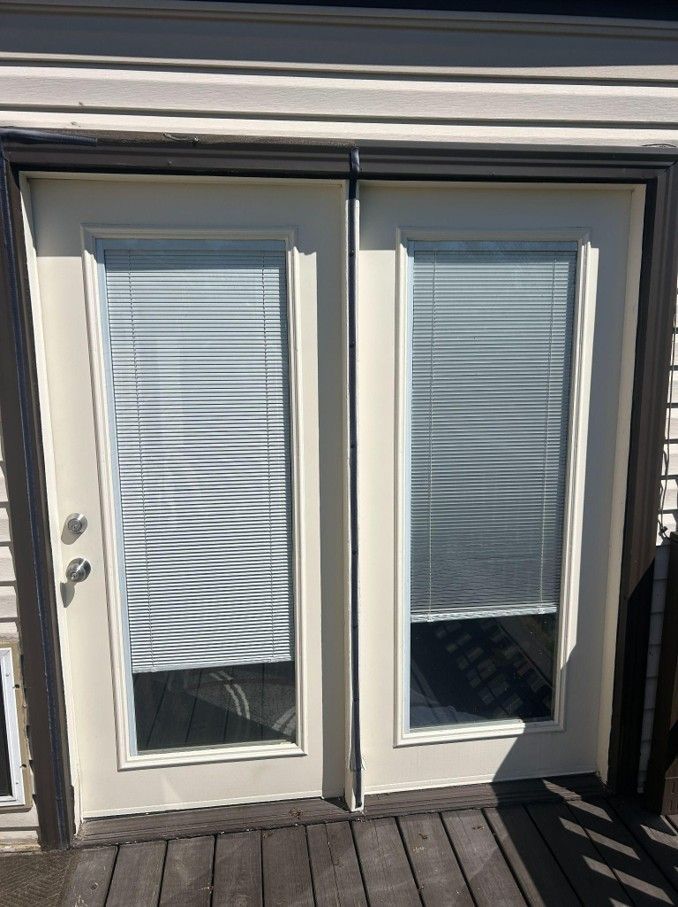 Double white French doors with closed blinds, viewed from a wooden deck.