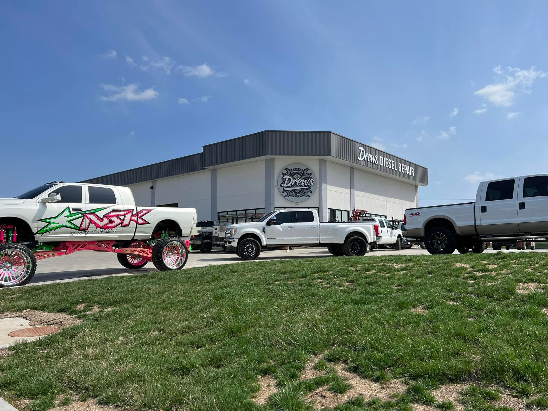Lifted trucks parked outside a warehouse under a blue Drew's | Drews Diesel Repair