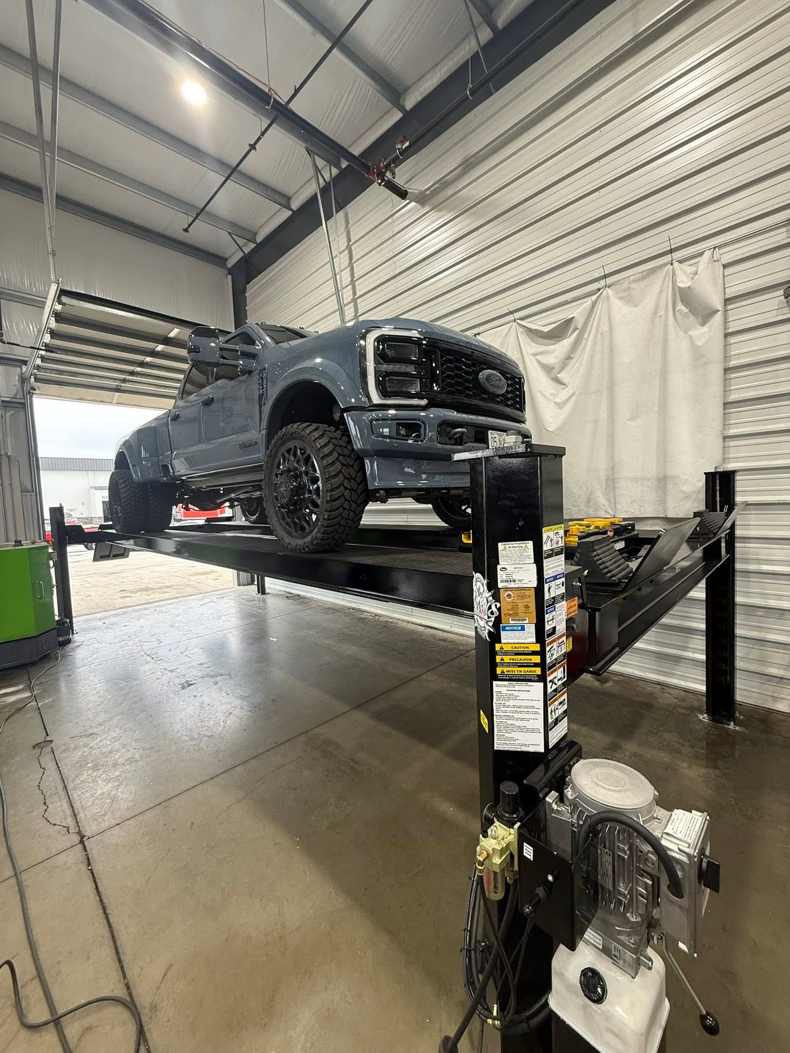Black pickup truck on a lift inside an auto repair Drew's | Drews Diesel Repair