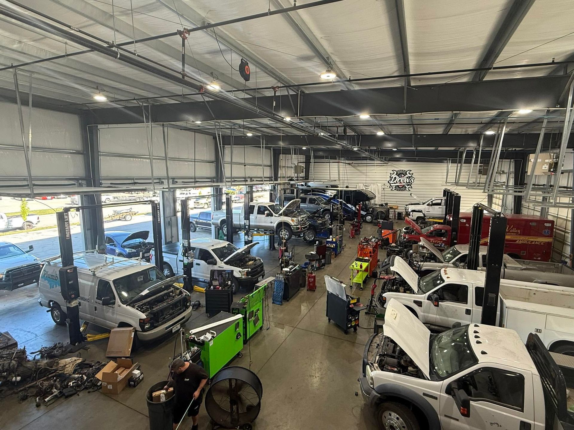 Inside a large auto repair shop, several vehicles are parked under bright industrial lights Drew's Diesel Repair