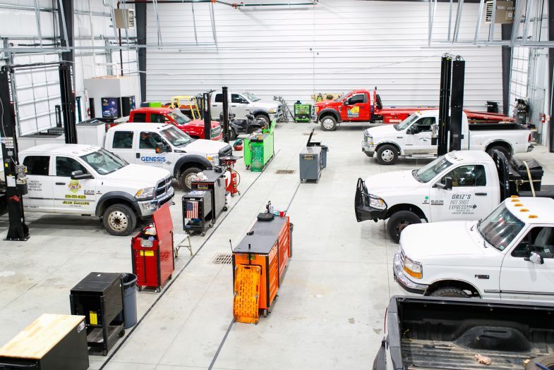 Auto repair shop with several white pickup trucks and service equipment in a large Drew's | Drews Diesel Repair