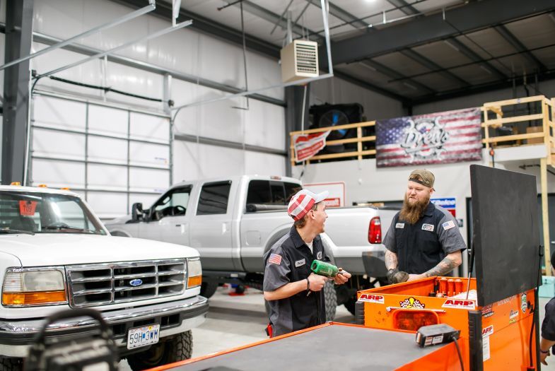 Two mechanics talking in a garage beside a silver pickup and orange tool cart | Drews Diesel Drew's