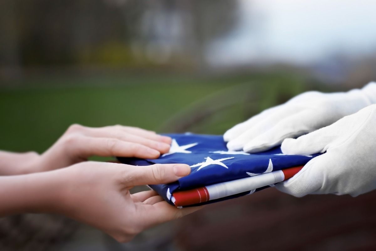 Hands passing a folded American flag in a solemn outdoor ceremony