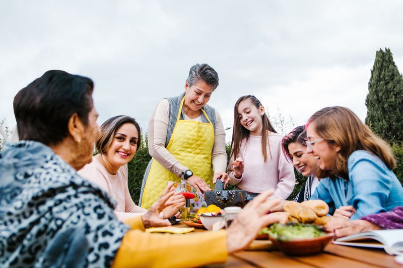 Friends gathered around an outdoor table sharing a meal and smiling in a garden setting
