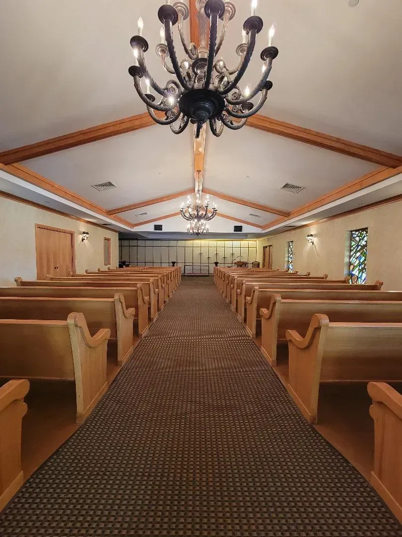 Empty church aisle with wooden pews, chandelier lights, and a central path leading to the altar.