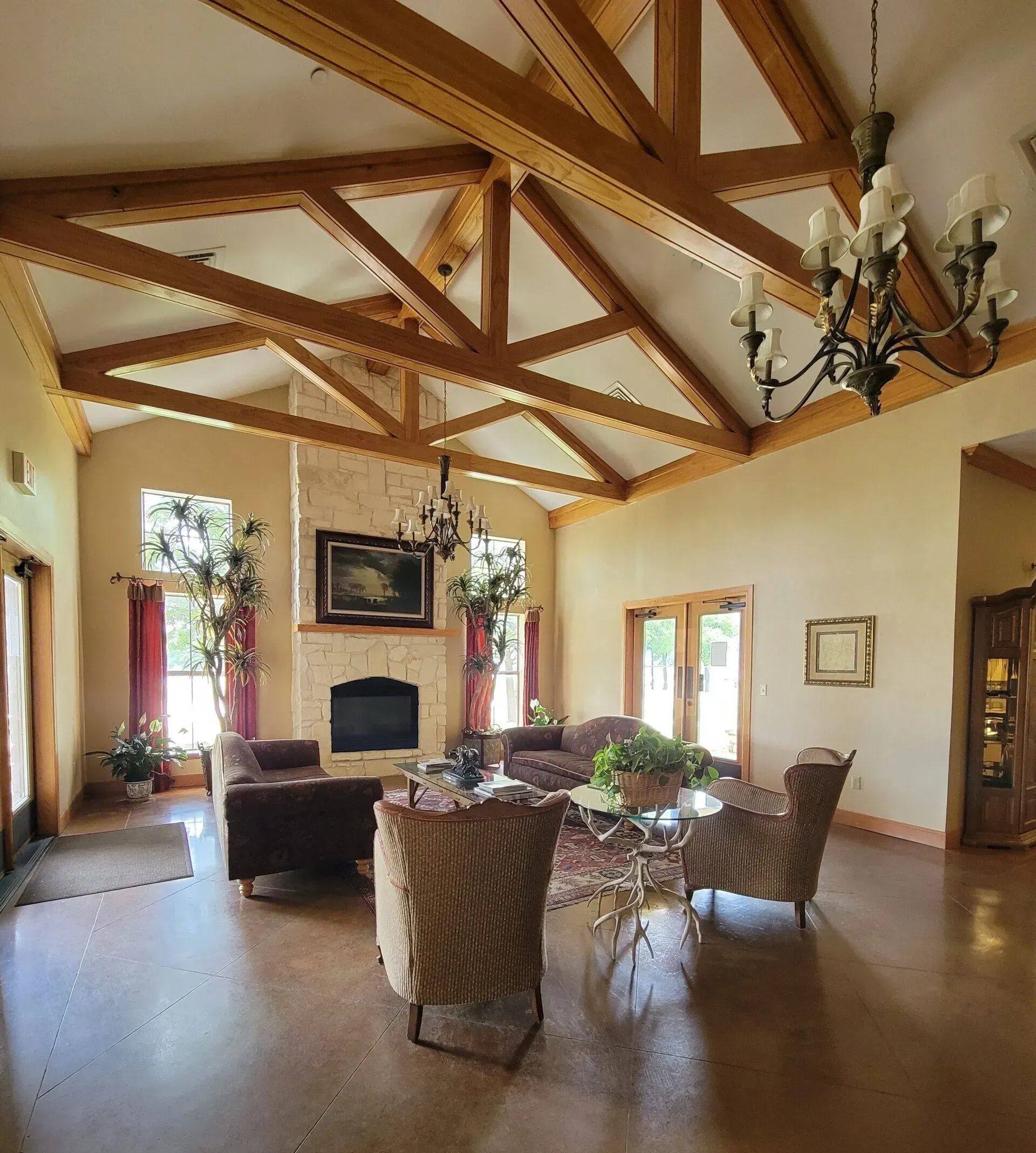 Elegant living room with exposed wood beams, chandelier, fireplace, and wicker chairs around a dining table.