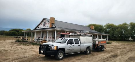 A silver work truck with a trailer parked in front of a house under construction with a newly shingled roof.