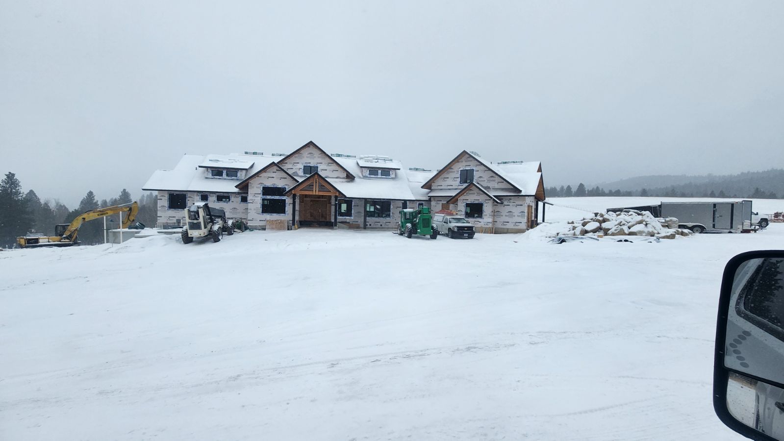 A partially built house under construction, surrounded by a snow-covered landscape with heavy machinery nearby.
