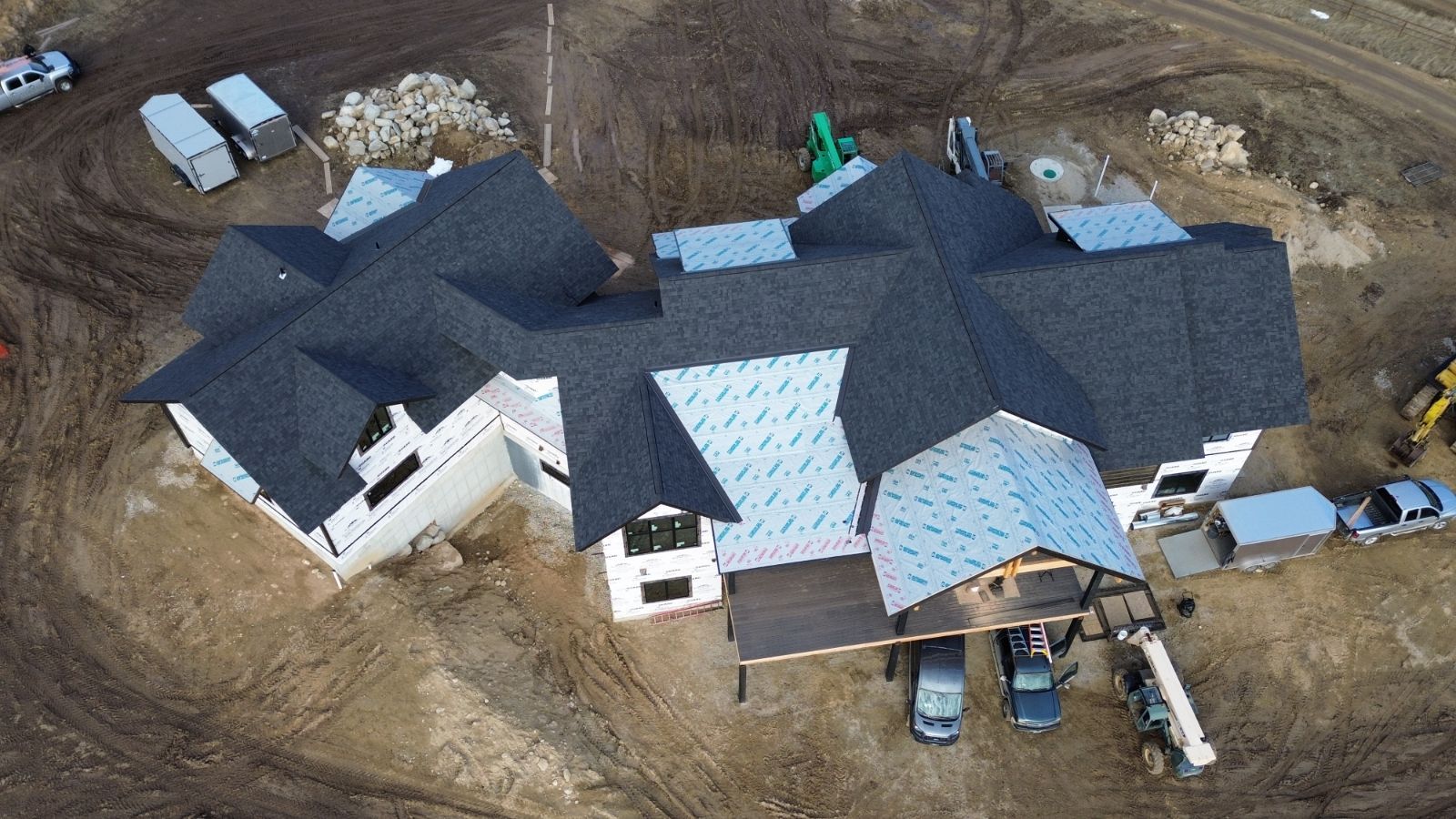 Aerial view of a large house under construction with a mix of shingled and underlayment-covered roof sections.