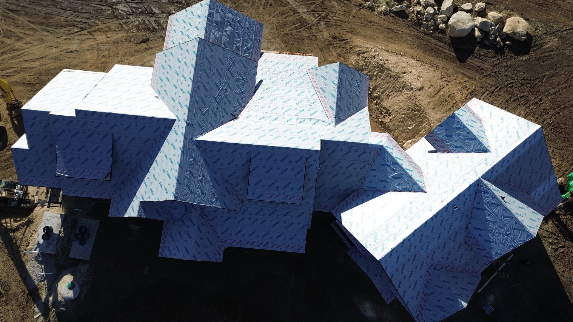An aerial view of a house frame under construction, completely covered in white, patterned insulation panels.