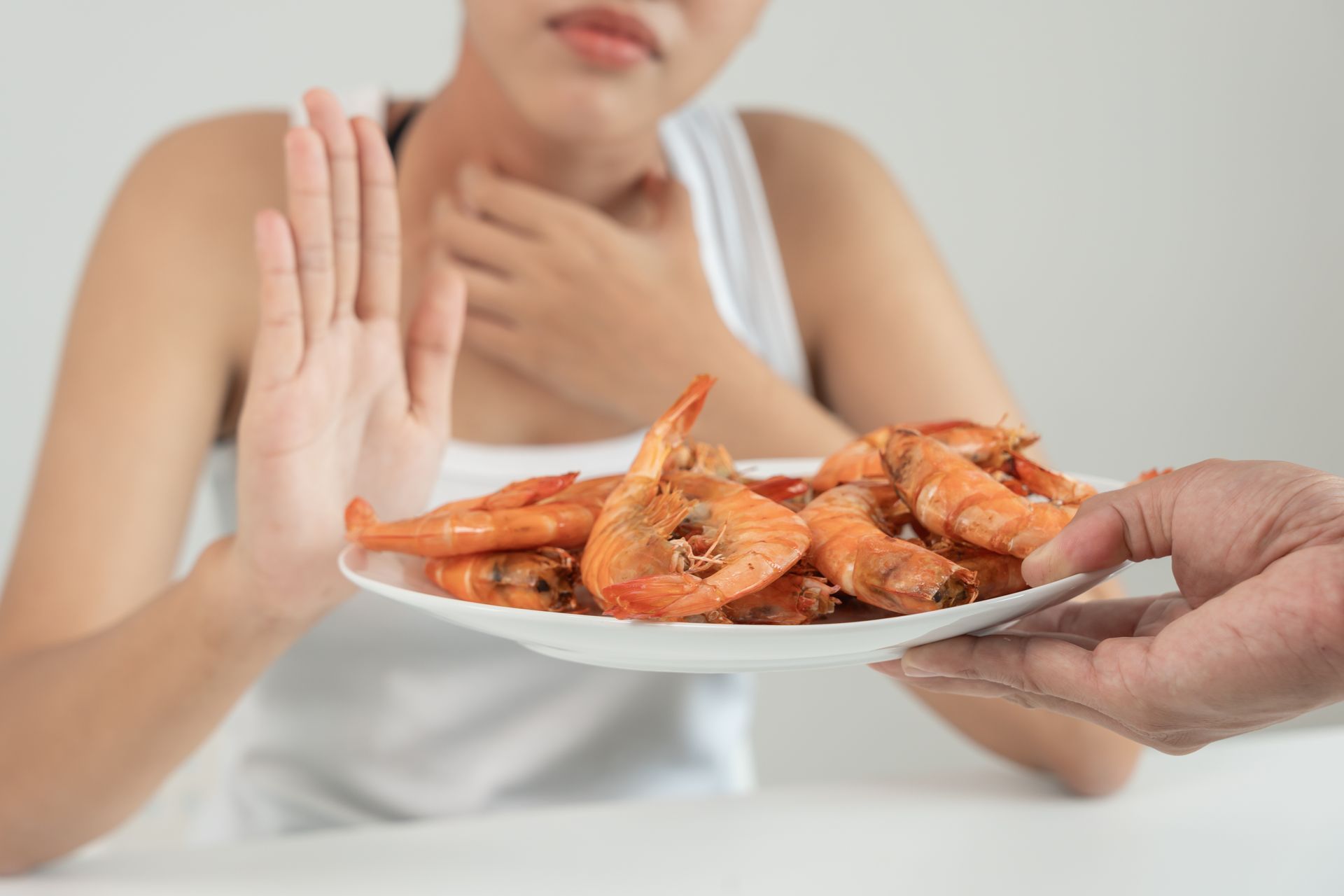 Person at table rejecting a plate of cooked shrimp with a raised hand