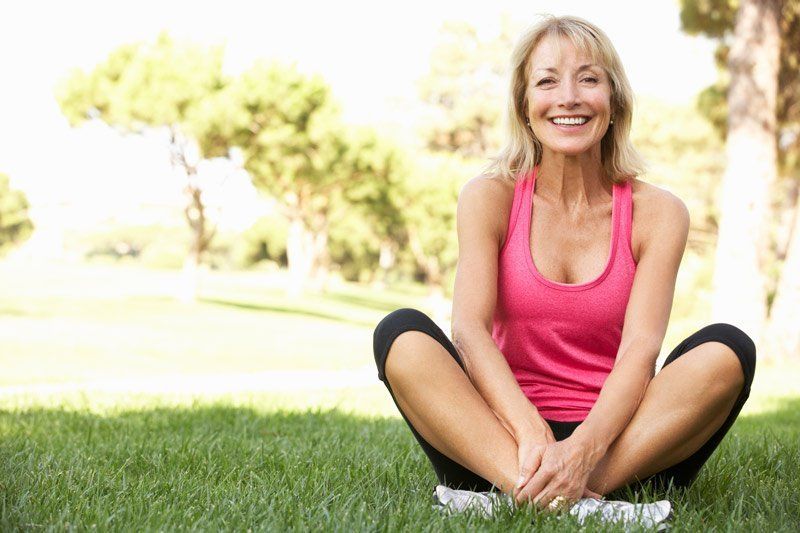 Smiling woman in a pink top sitting cross-legged on grass in a sunny park