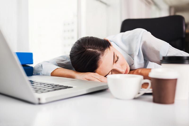 Person asleep at a desk beside an open laptop and coffee cups