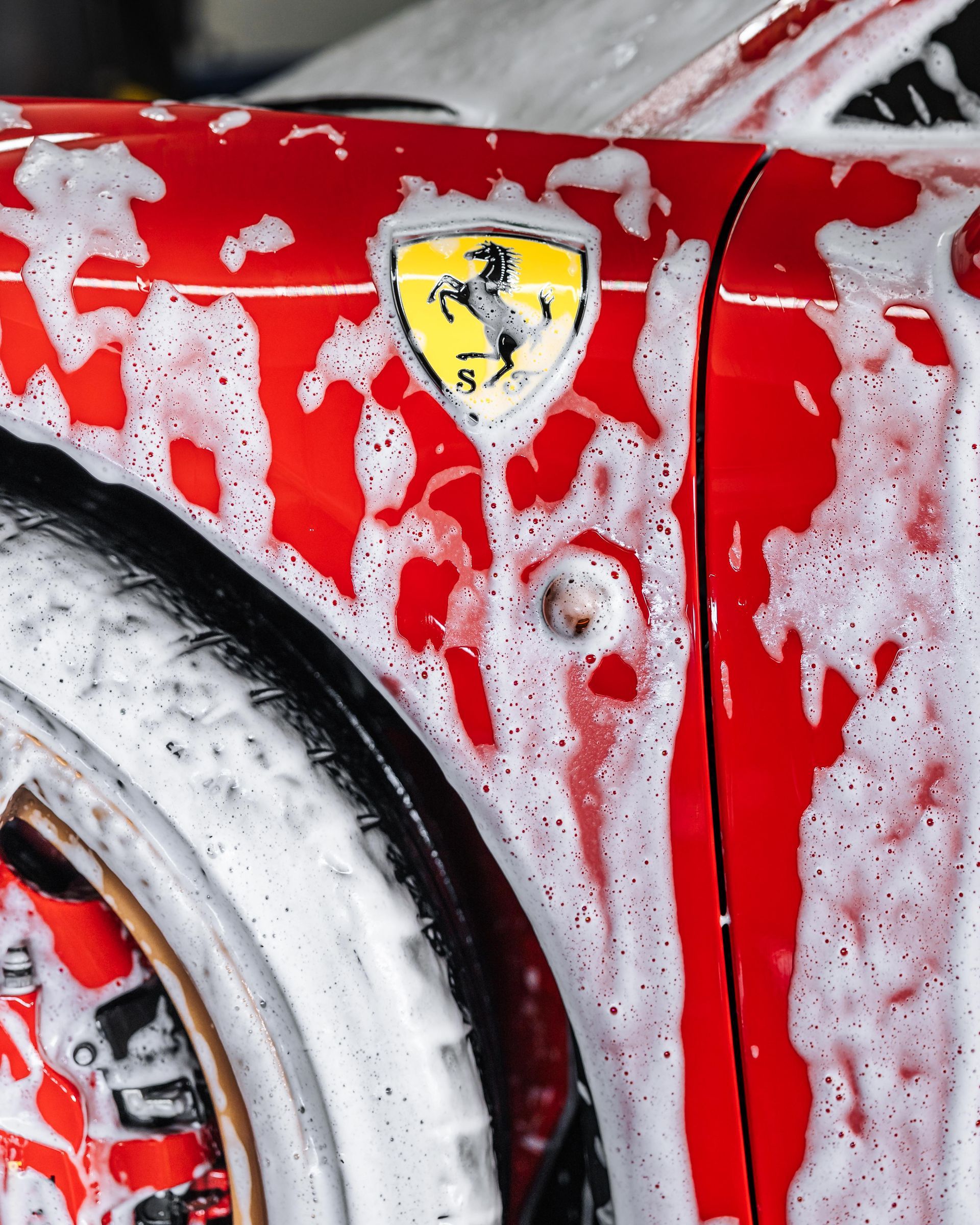Close-up of a red Ferrari covered in soap suds during a car wash