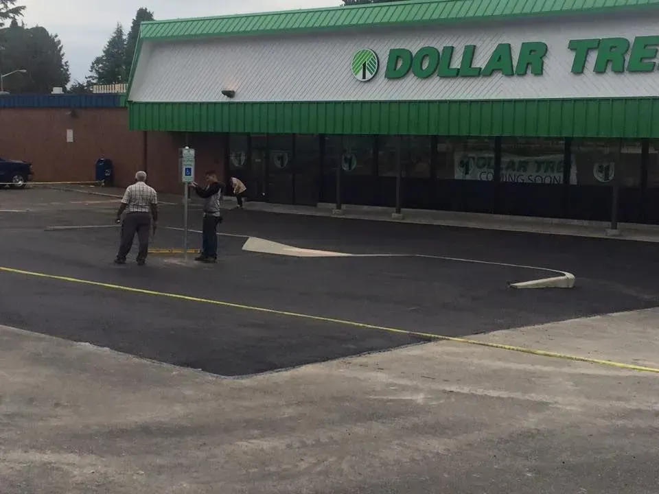 Dollar Tree store exterior with two people near a parking area. Green and white building with a paved parking lot.