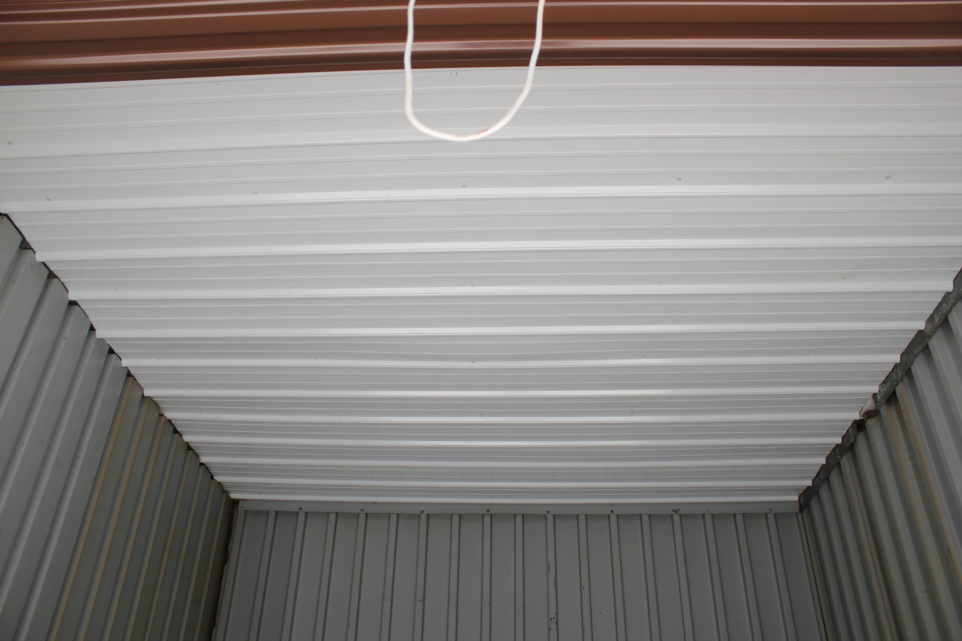 White corrugated ceiling inside a metal storage container, with a hanging cord visible near the top. White corrugated ceiling inside a metal storage container, with a hanging cord visible near the top.
