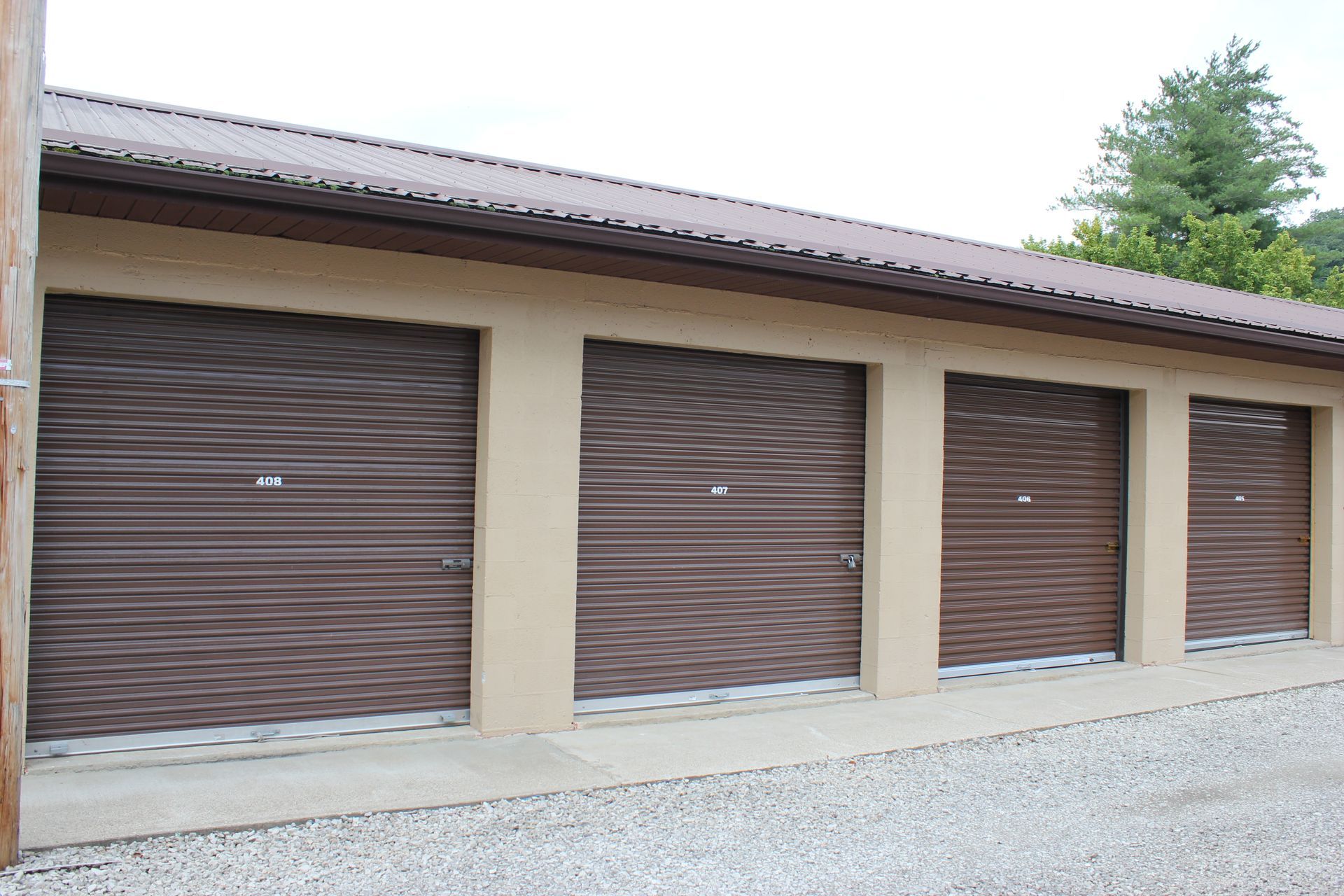 Row of brown storage unit doors on a beige building with a gravel lot in front Row of brown storage unit doors on a beige building with a gravel lot in front