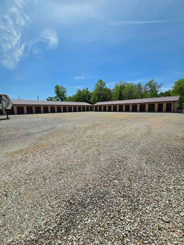 Wide gravel lot in front of long beige storage units under a bright blue sky. Wide gravel lot in front of long beige storage units under a bright blue sky.