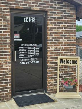 Brick office entrance with glass door, number 7433, and a “Welcome” sign beside potted flowers. Brick office entrance with glass door, number 7433, and a “Welcome” sign beside potted flowers.