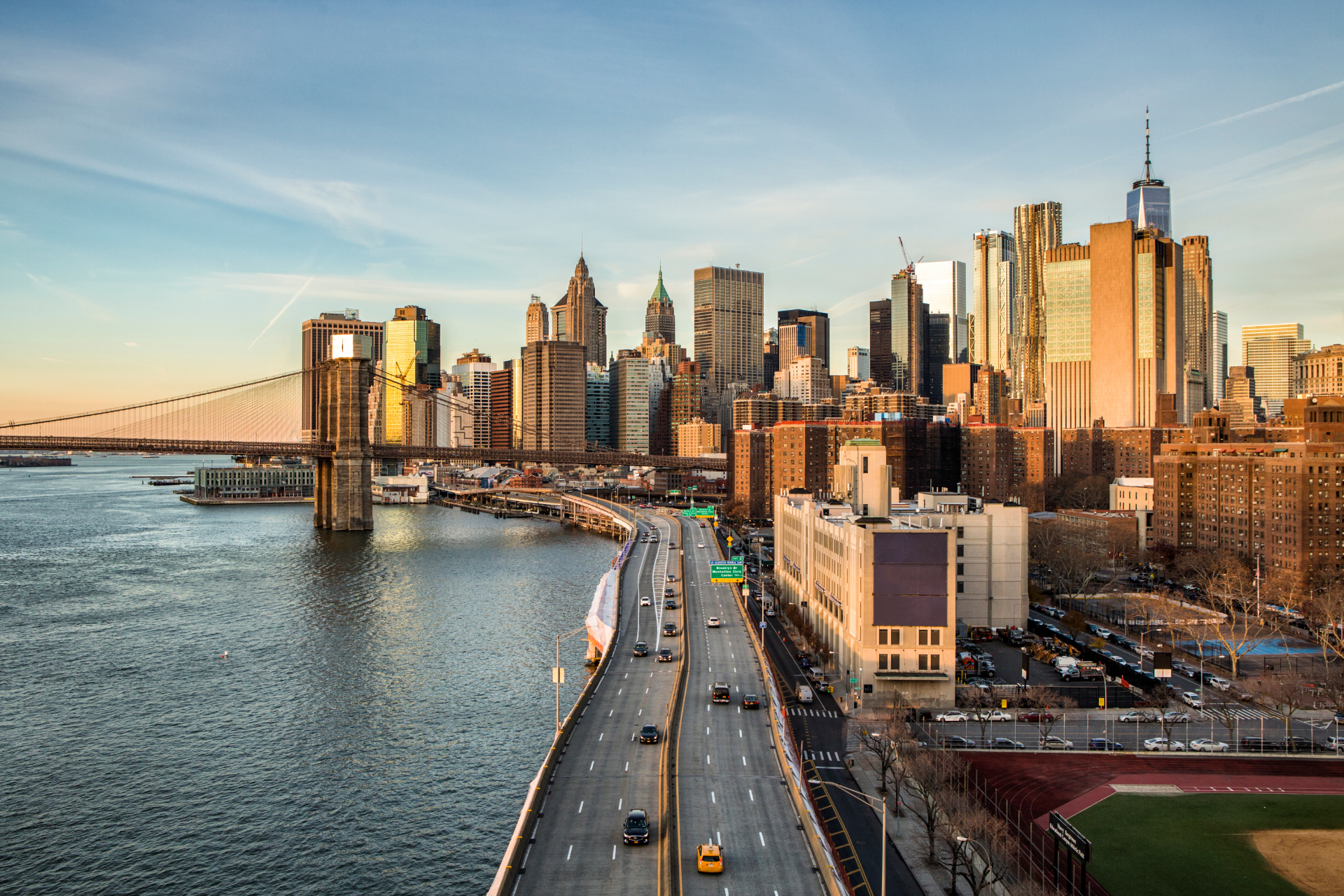 New York City skyline at golden hour with the Brooklyn Bridge and FDR Drive along the East River.