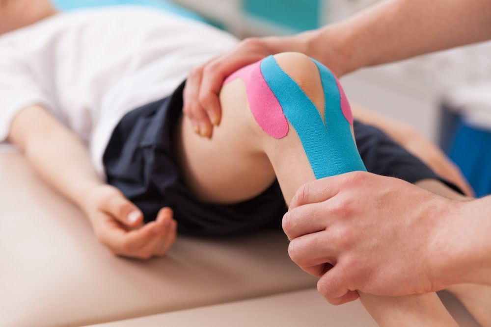 A person is putting kinesio tape on a knee.