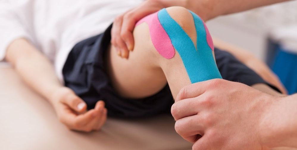 A person is applying kinesio tape to a child 's knee.