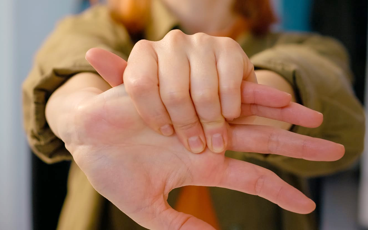 Hands demonstrating a sign gesture against a blurred indoor background