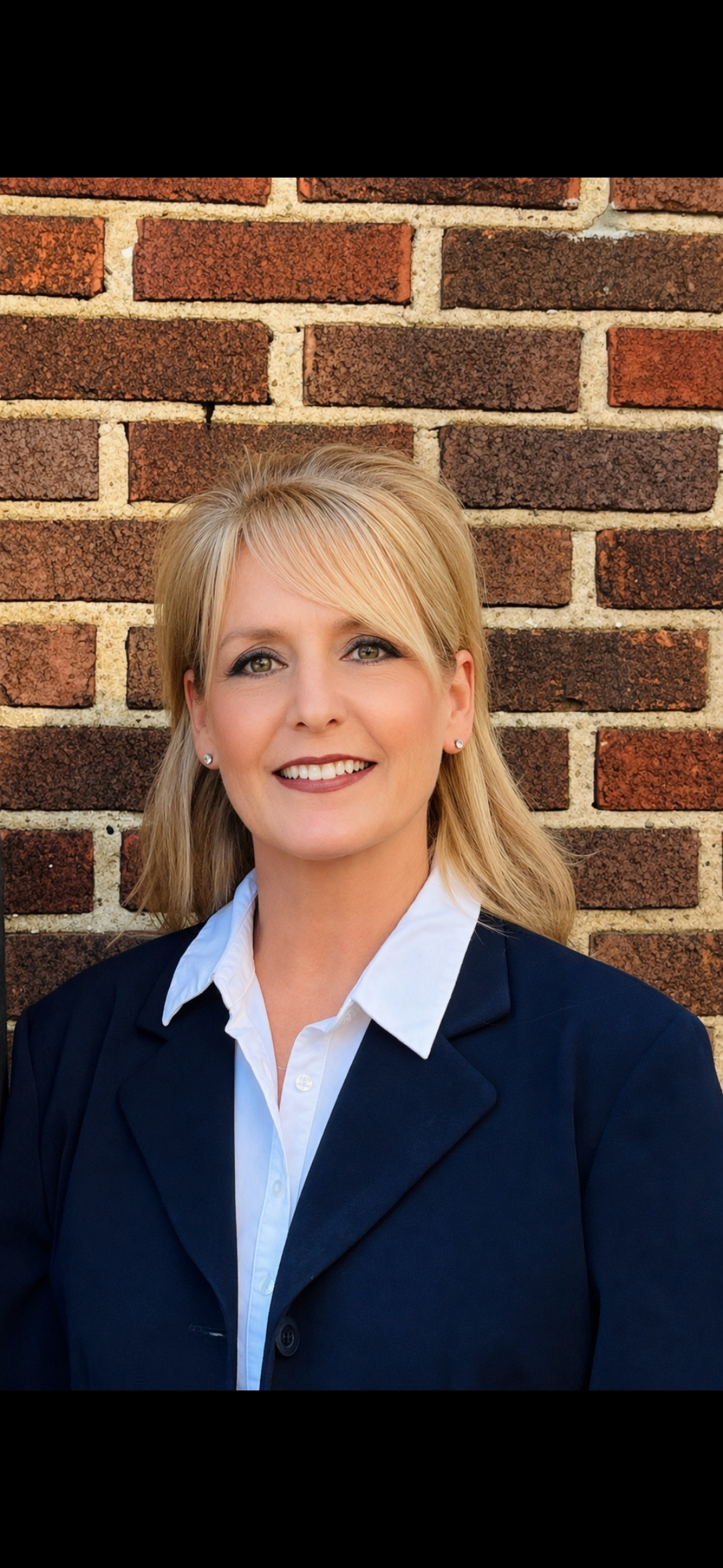 Smiling woman in a navy blazer standing against a brick wall
