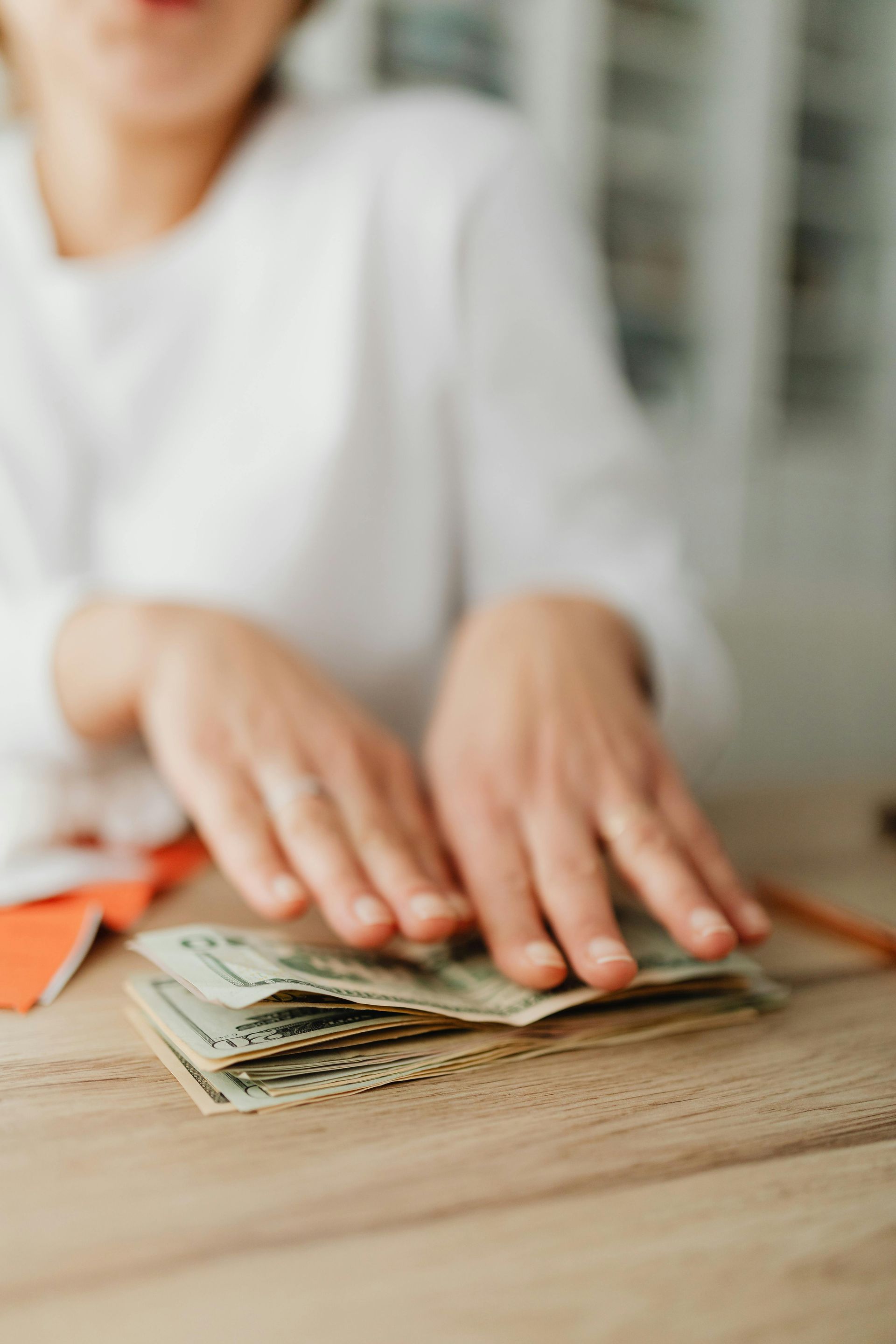 Hands counting cash on a wooden table with orange envelopes nearby