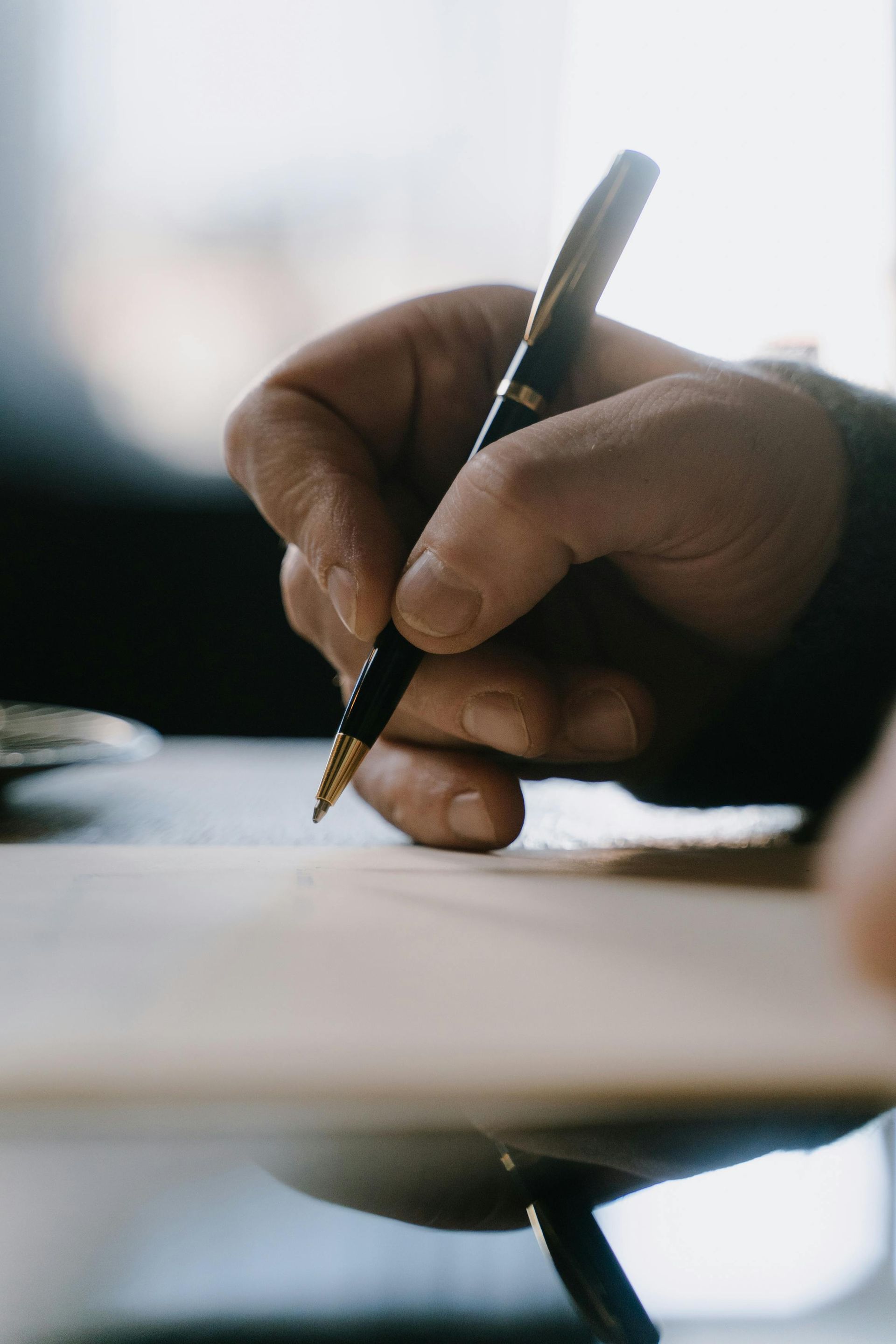 Hand writing with a pen on paper, close-up of a hand in warm light