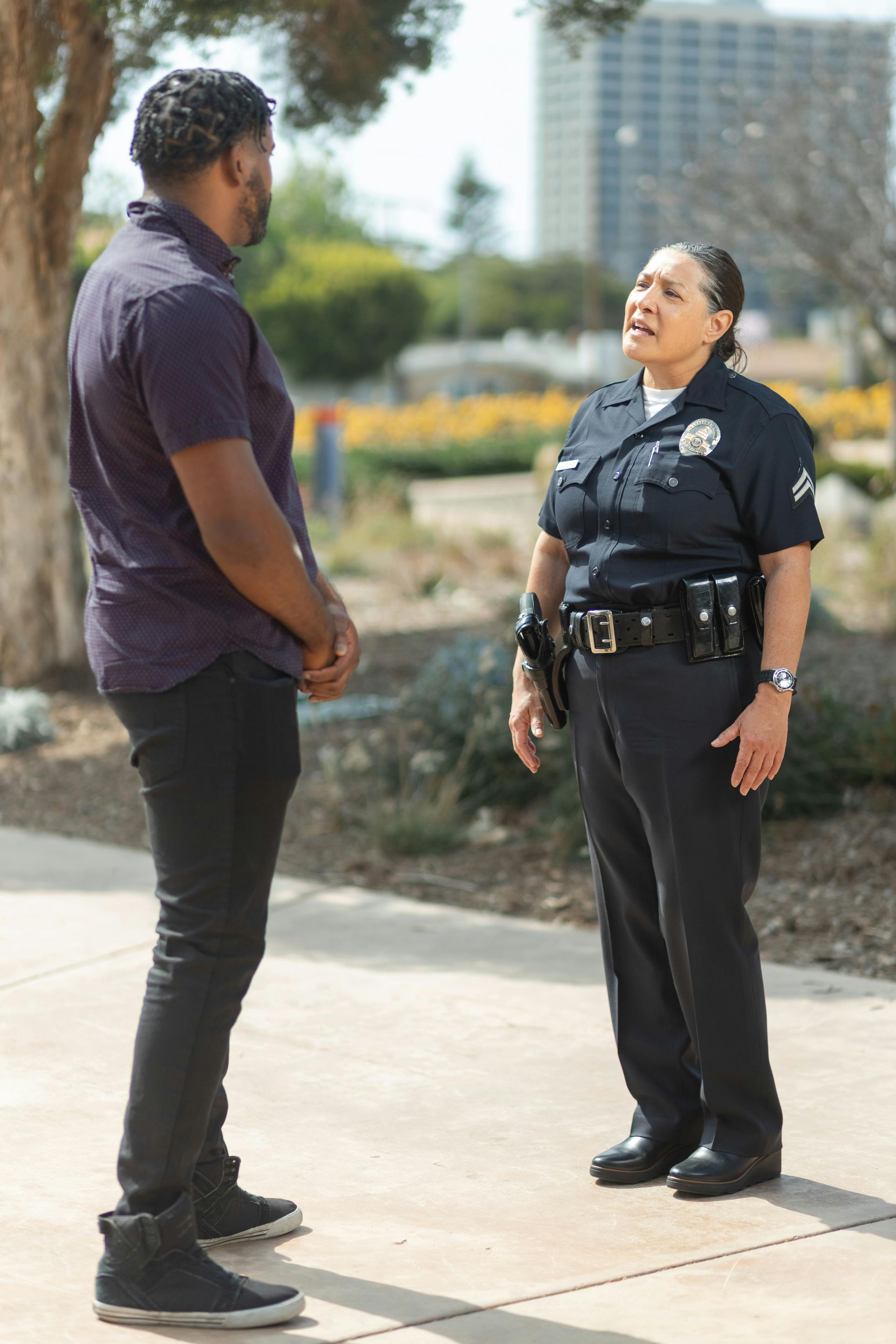 Police officer speaking with a man outdoors on a sidewalk near a building and flowers.