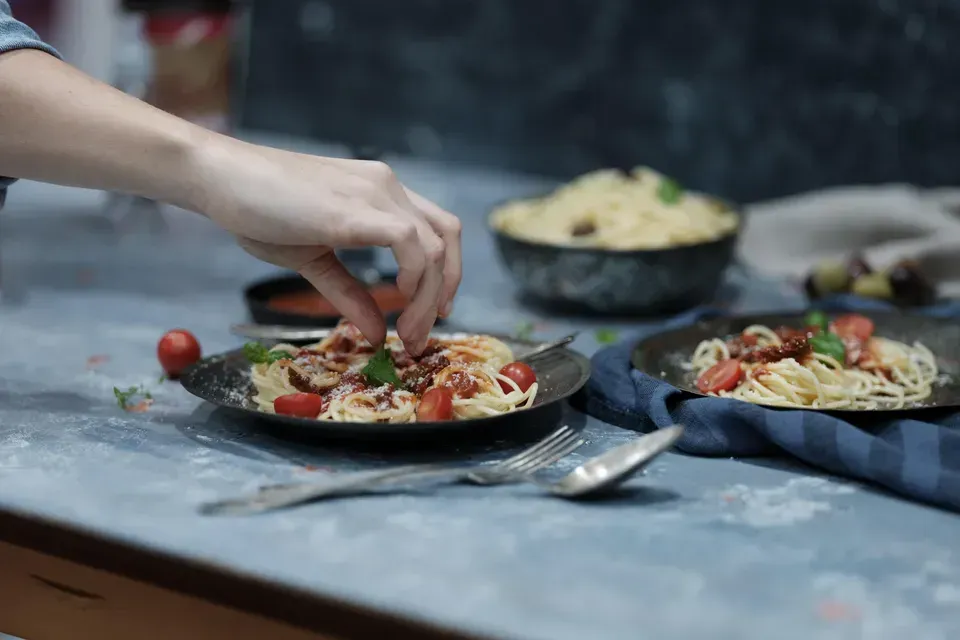 A person is putting tomatoes on a plate of spaghetti