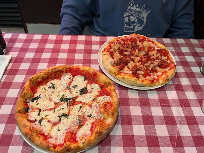 Two personal pizzas are sitting on a checkered tablecloth on a table