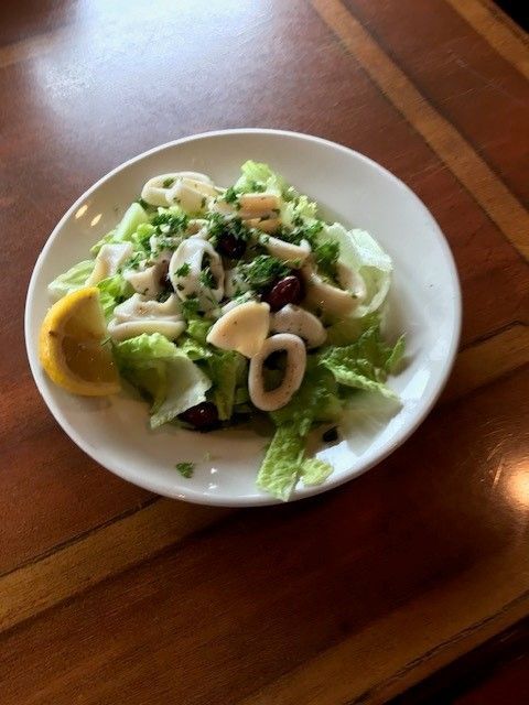 A white plate with a seafood salad and slice of lemon on it