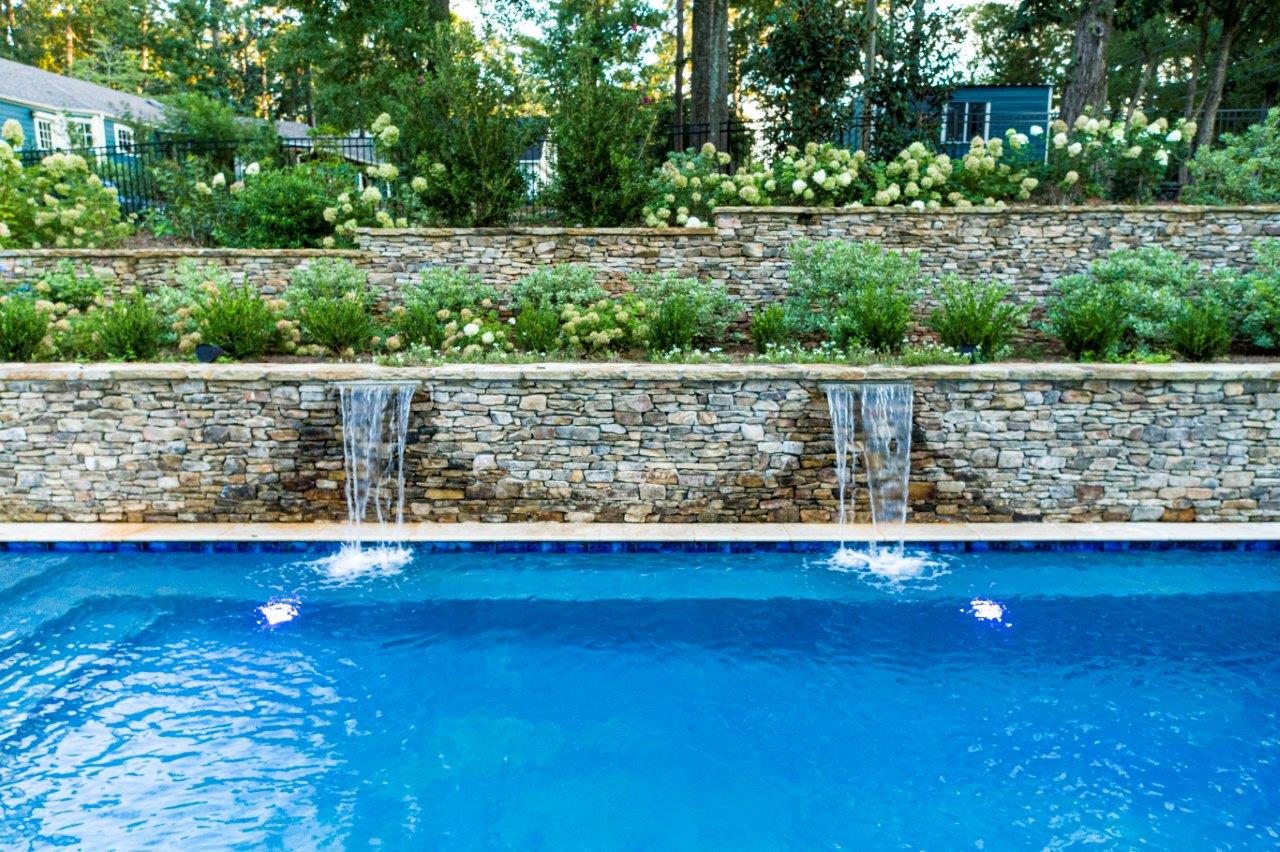 A pool with stone waterfalls and a tiered garden with flowers; blue water.
