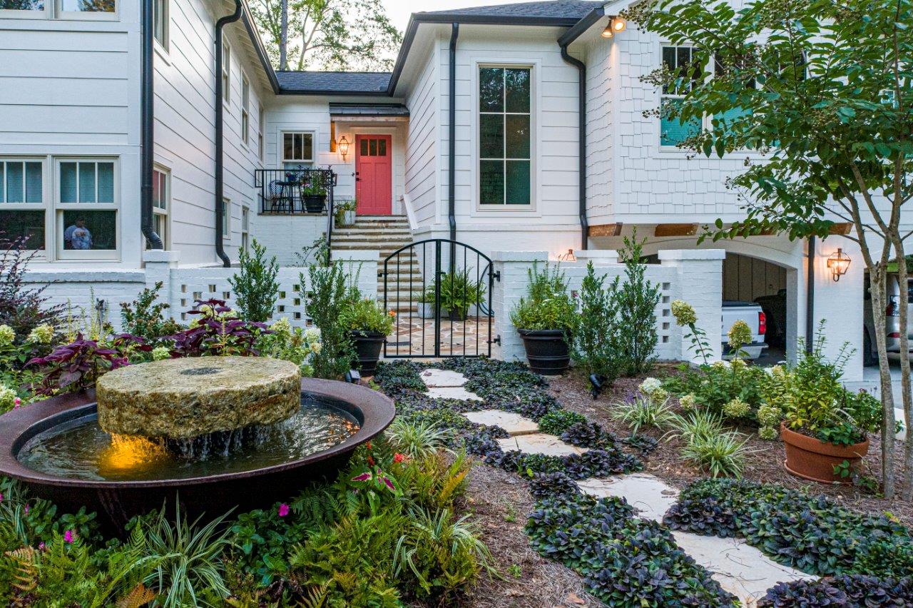White house with coral door, stone path, fountain, and gate leading to entrance.