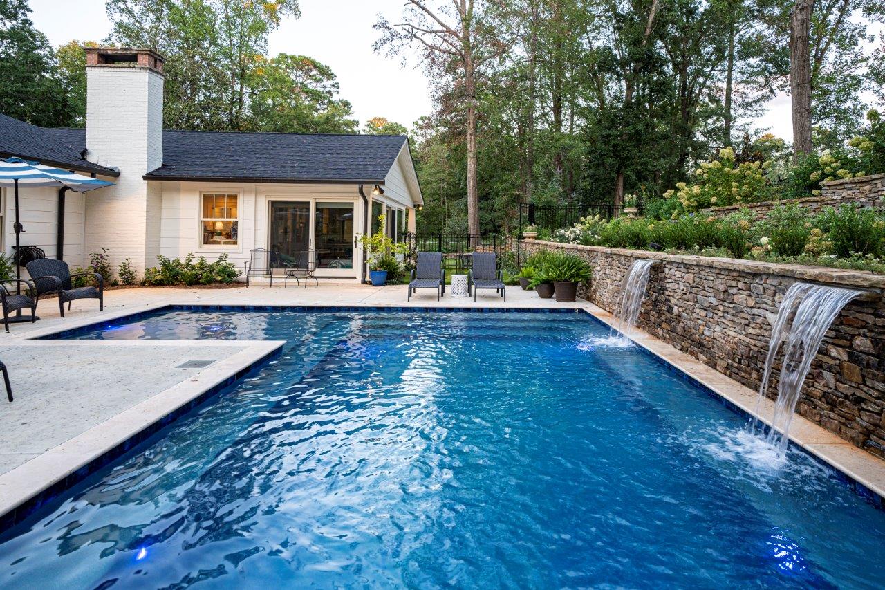 Backyard pool with a stone waterfall feature. House with a white exterior in the background.