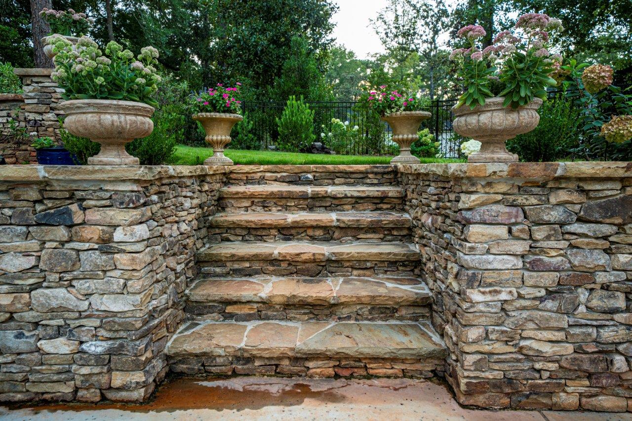 Stone steps lead up to a garden with urns filled with flowers.