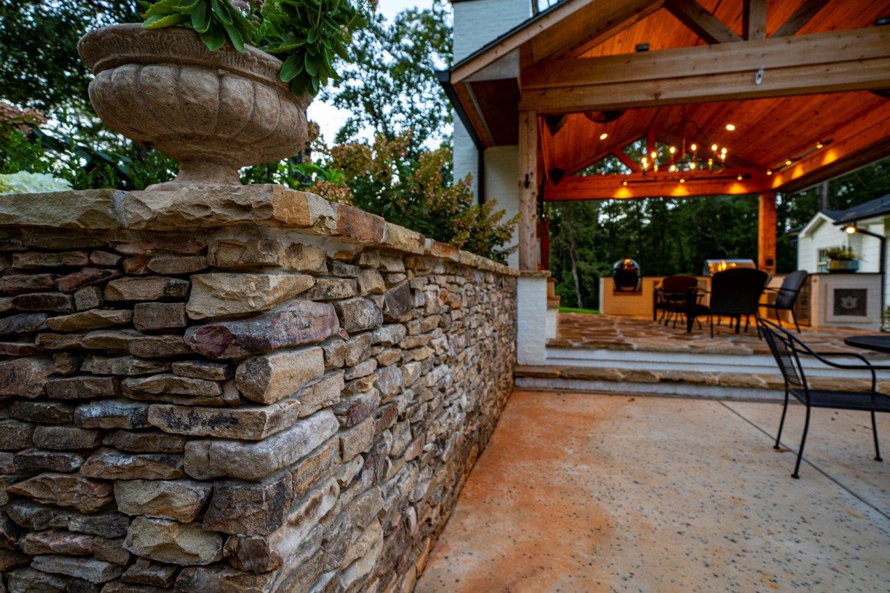 Stone wall with a patio, covered porch with string lights, and outdoor seating.